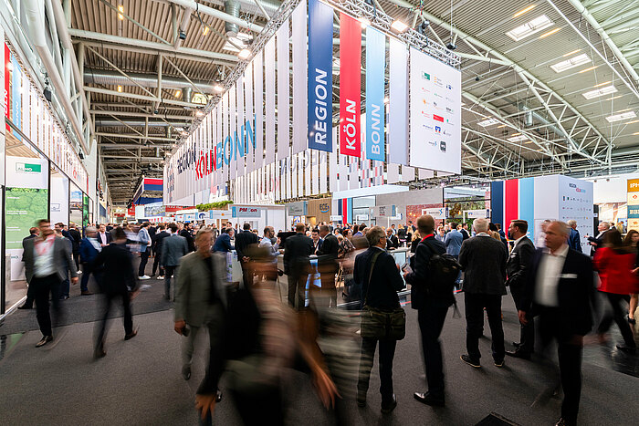 Menschen vor einem Messestand in einer großen Messehalle.