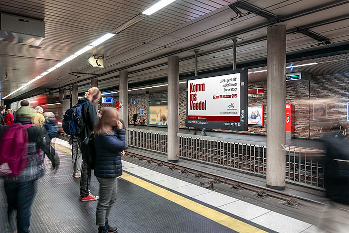 Menschen an einem U-Bahnhof vor einer Werbetafel.